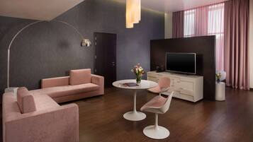A modern living room with a sofa, two chairs, a round table, a TV, and a large window with curtains.