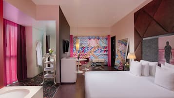 A modern hotel room with a large bed, a desk with a chair, a vanity with a mirror, and a colorful wall mural.
