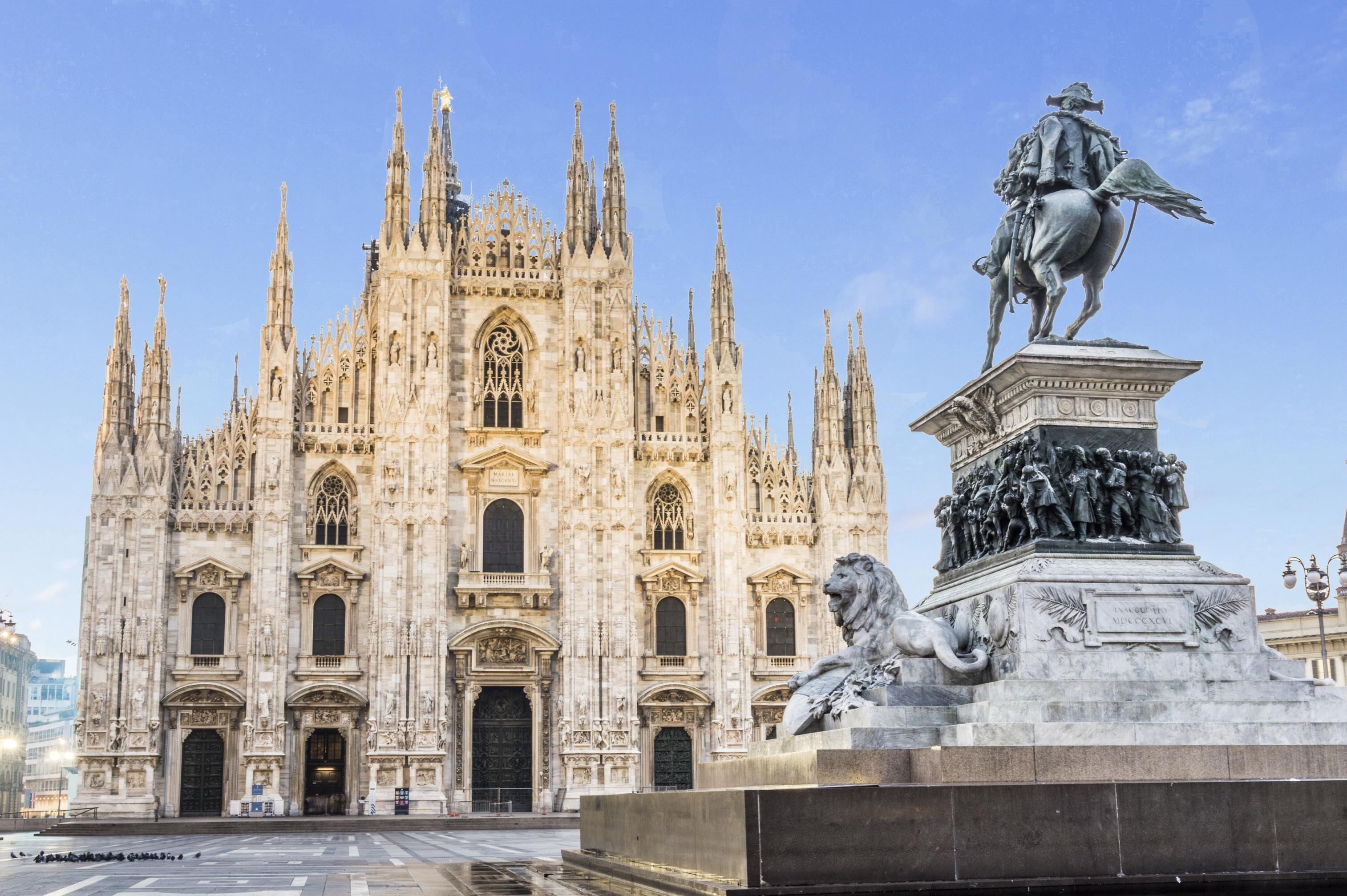 A grand cathedral with intricate Gothic architecture, a prominent statue of a historical figure on horseback, and a lion sculpture at its base.