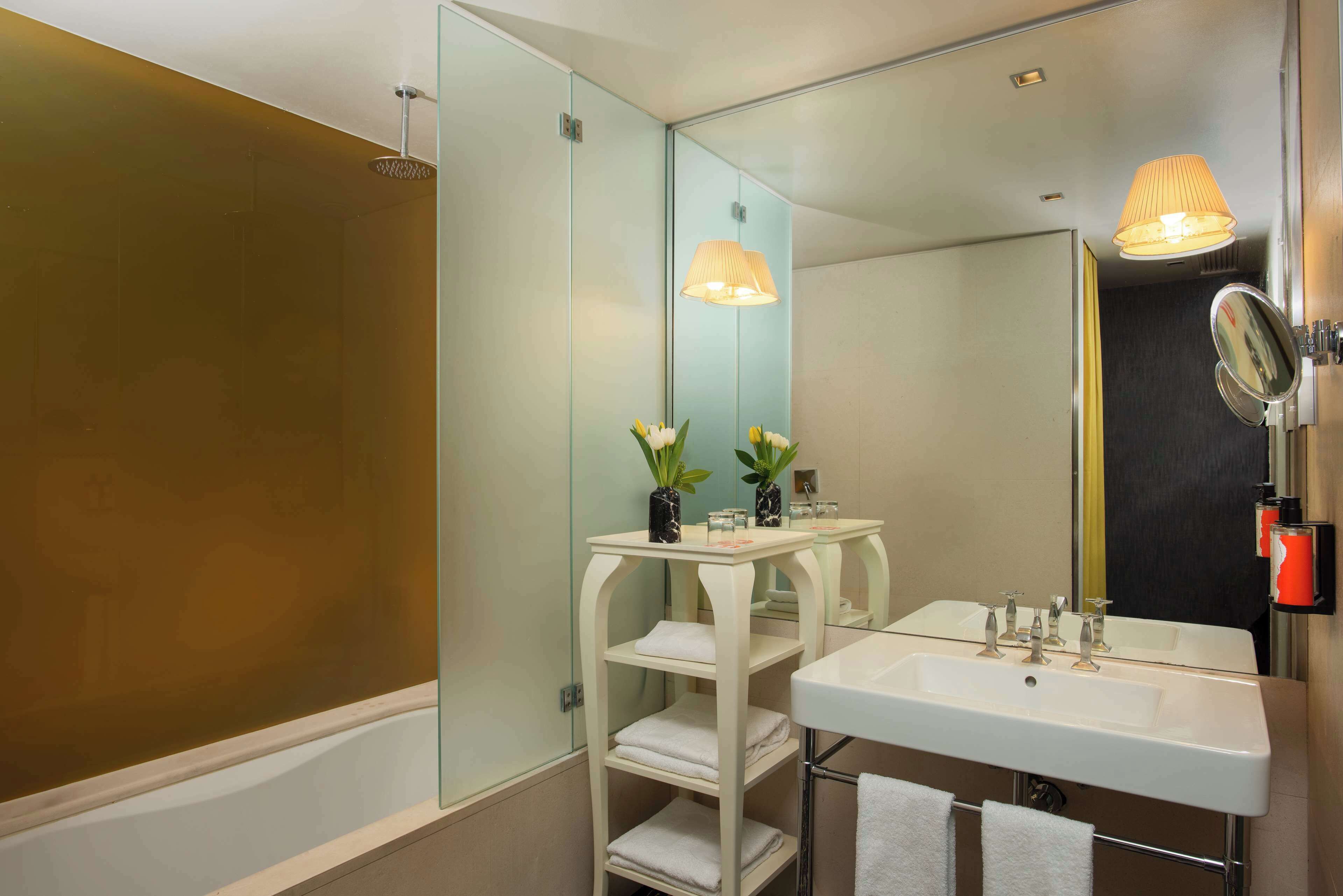 A modern bathroom with a bathtub, a large mirror, a sink, and a shelf with towels and toiletries.