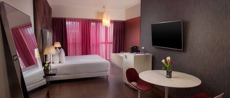 Una habitación de hotel moderna con cama, mesita de noche, lámpara y una pequeña mesa redonda con dos sillas.