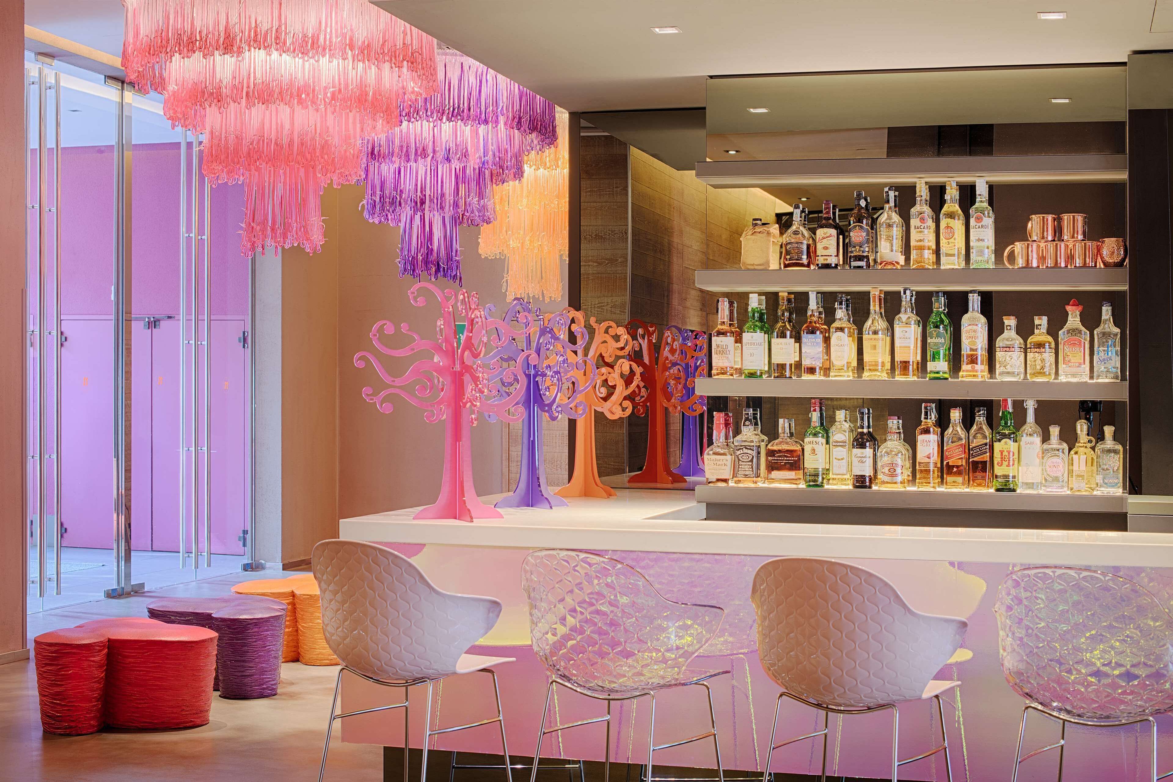 A bar area with a variety of liquor bottles, colorful chairs, and a decorative tree sculpture.