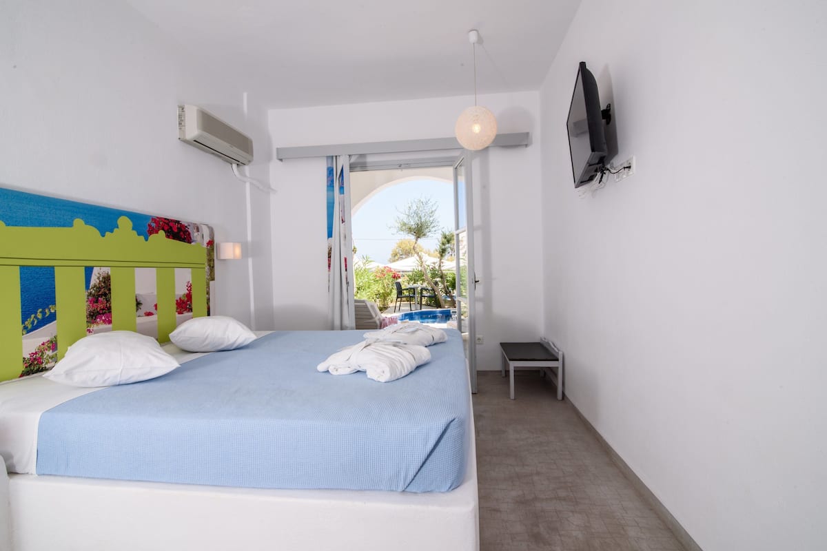 Un dormitorio con cama, paredes blancas, televisor montado en la pared y aire acondicionado.
