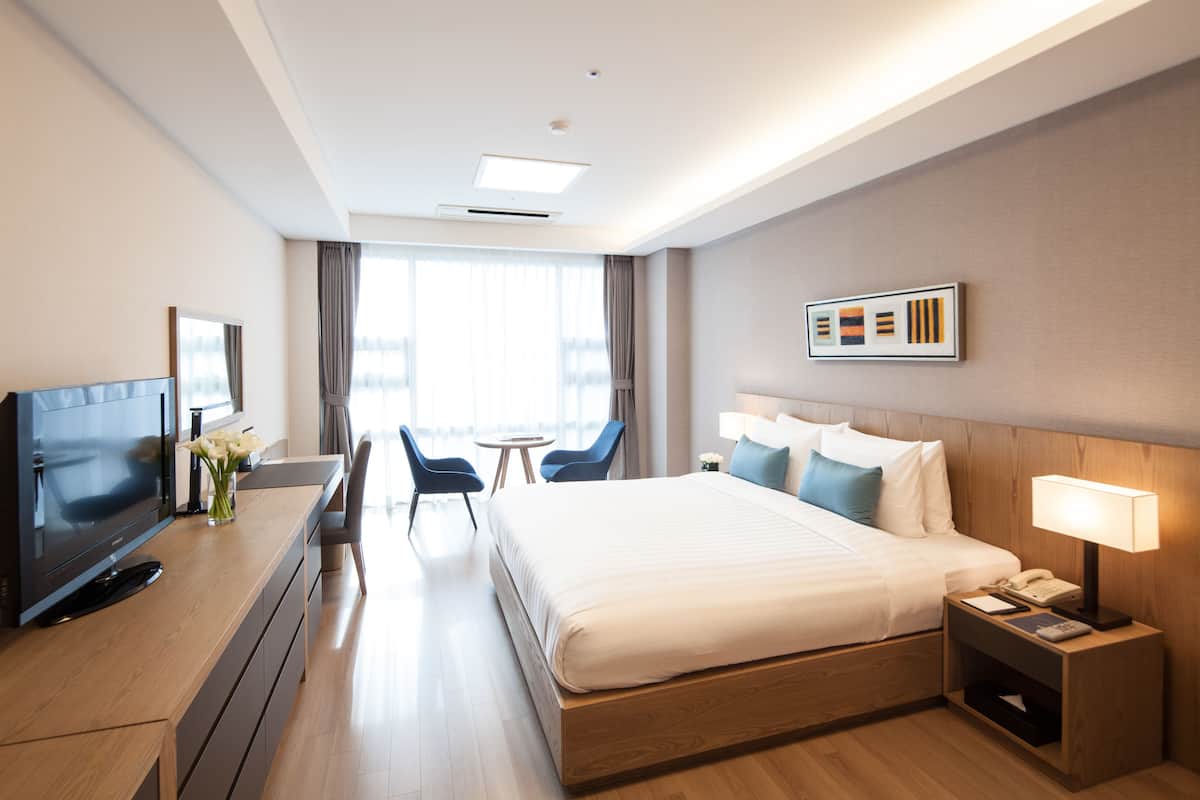 Una habitación de hotel con cama, mesita de noche, lámpara, televisor y escritorio con silla y flores.