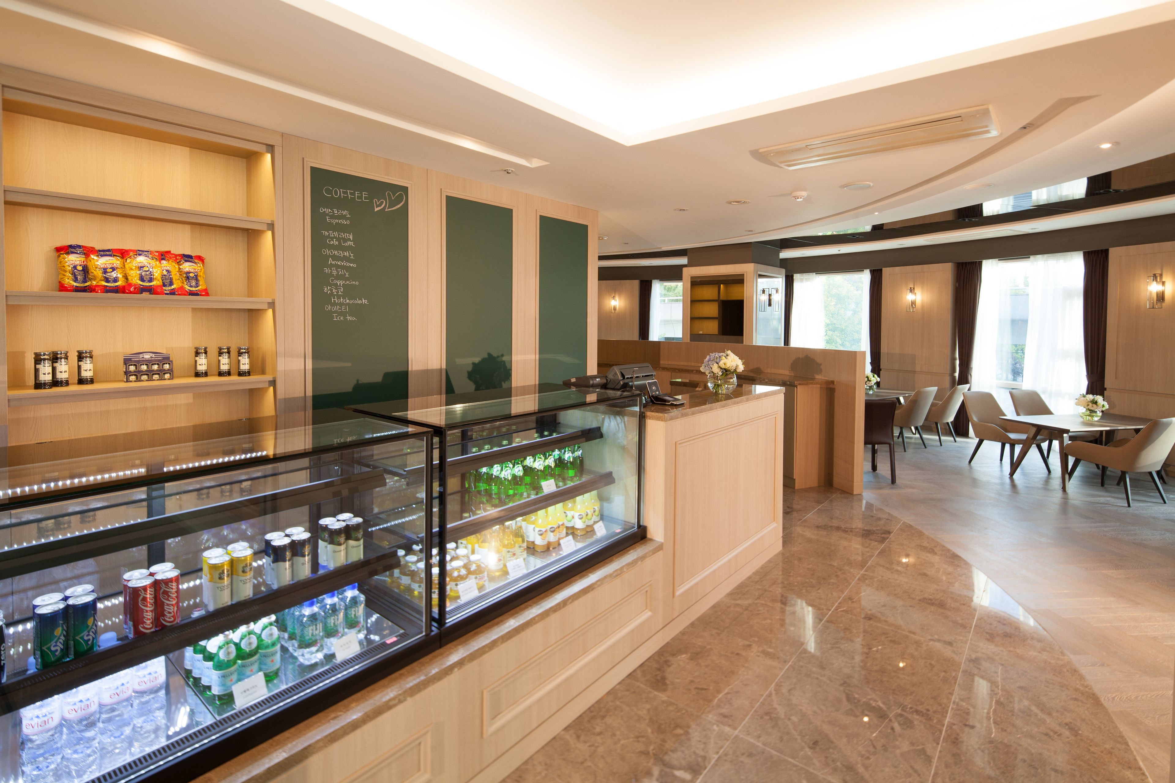 A modern hotel lobby with a coffee station, seating area, and a glass display case with snacks.