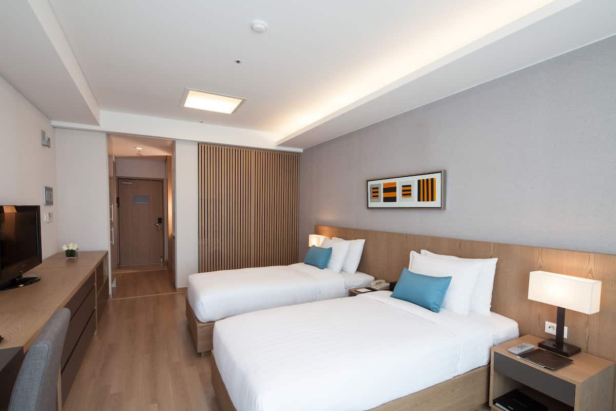 Habitación de hotel con dos camas, un escritorio, un televisor y una obra de arte colgada en la pared.