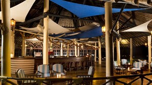 Un área de estar interior con mesas y sillas, un bar y vistas al área de la piscina.