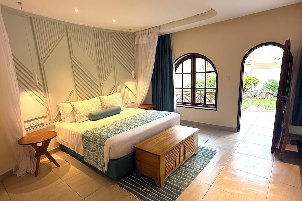 Quarto moderno com cama, mesa de cabeceira, banqueta e grandes janelas.