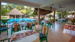 A poolside restaurant with tables and chairs, a pool, and thatched-roof structures. - Neptune Paradise Beach Resort & Spa (Diani Beach)