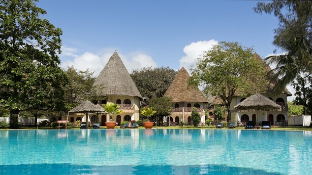 Un resort con piscina, edificios de techo de paja y abundante vegetación.