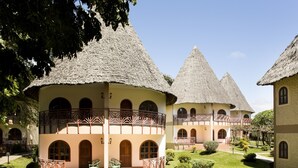 Un patio con edificios de techo de paja, una zona de estar central y un jardín bien cuidado.