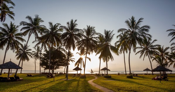 A beach with palm trees, sun loungers, and thatched umbrellas. - Neptune Paradise Beach Resort & Spa (Diani Beach)