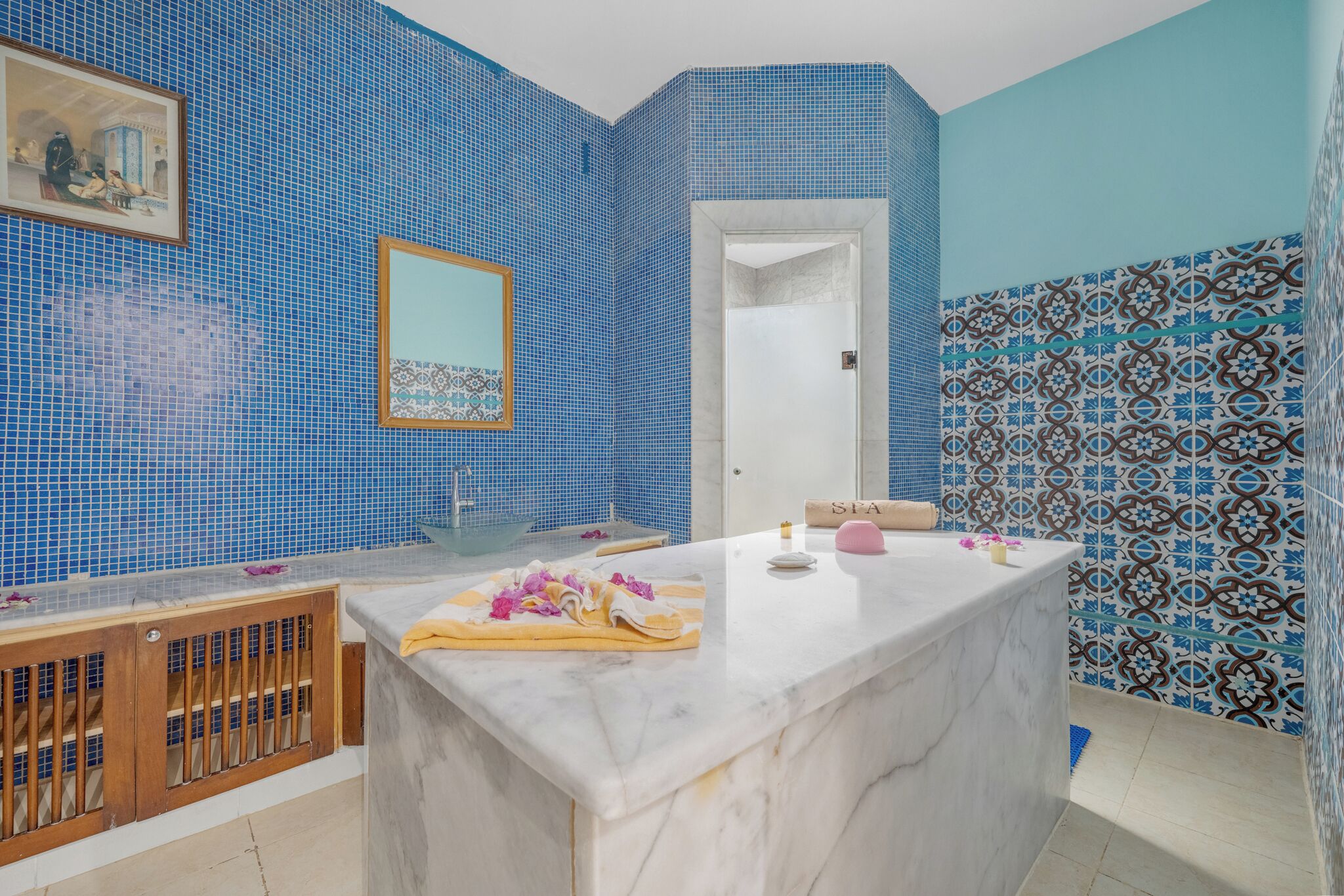 Ein Badezimmer mit blauen Mosaikfliesen, einem Marmorwaschbecken, einem Holzschrank und einem Spiegel.