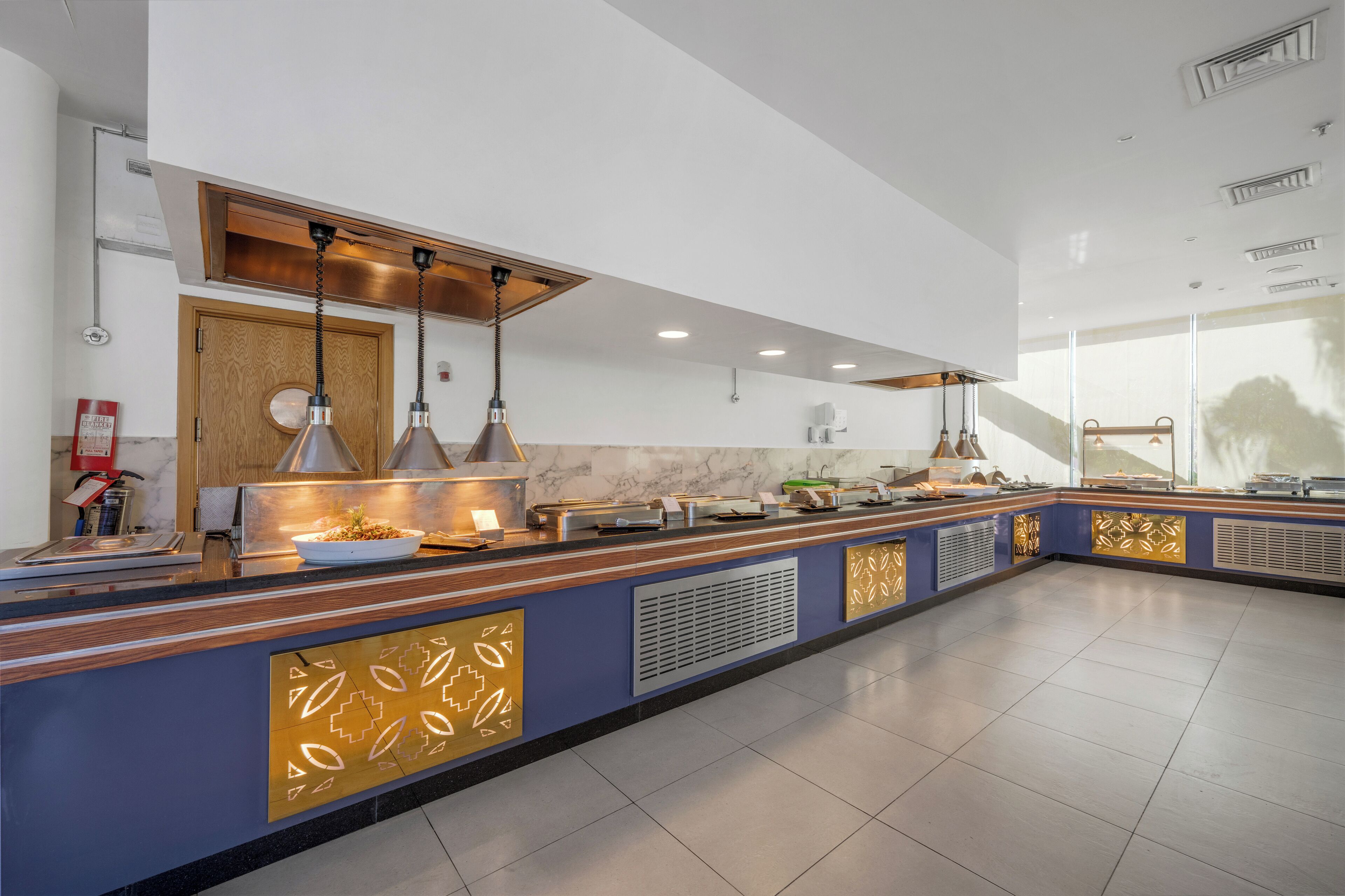 A modern kitchen with a long counter, pendant lights, and a fire extinguisher.