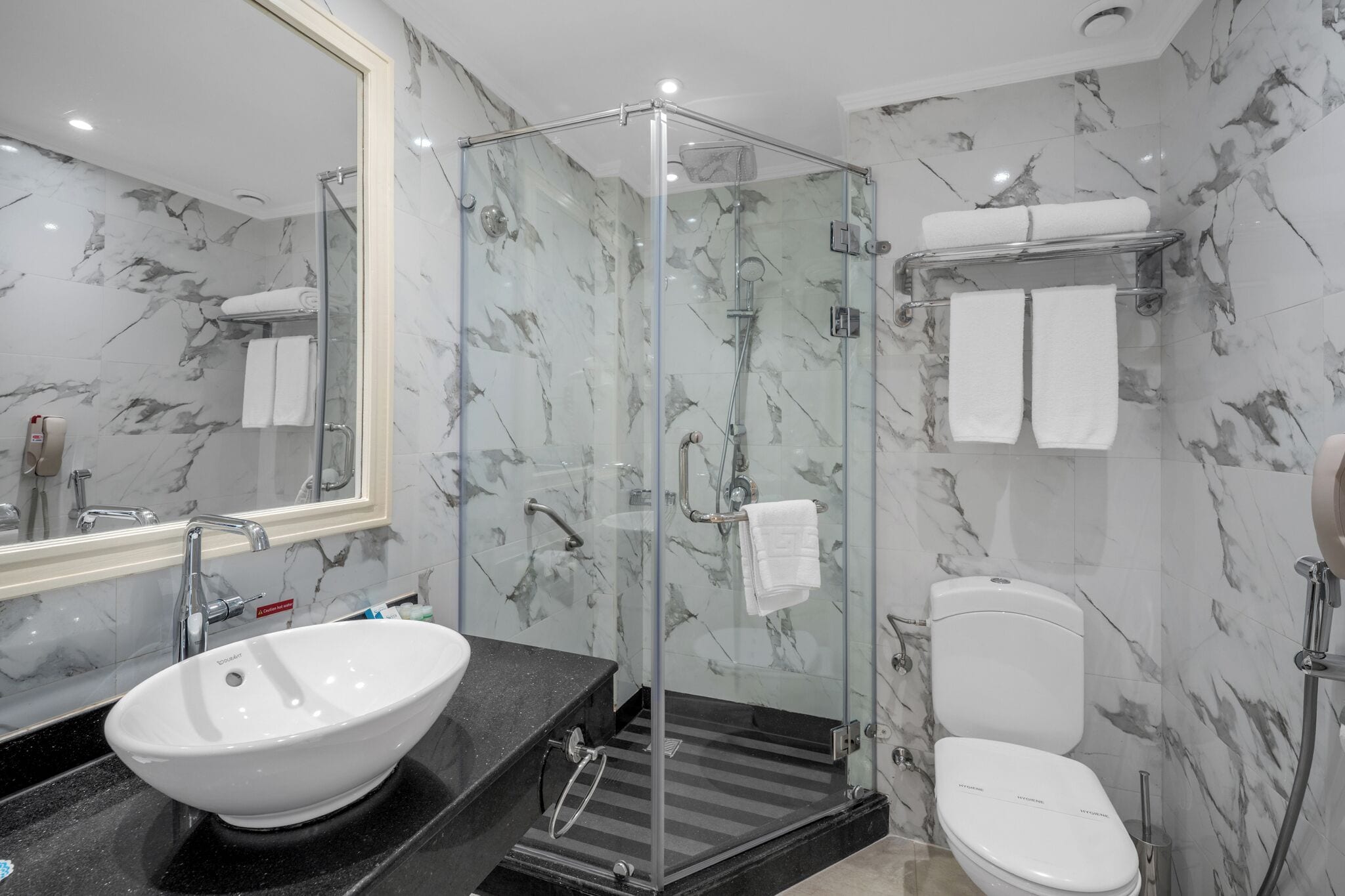 A modern bathroom with a glass-enclosed shower, a white sink, and a toilet.