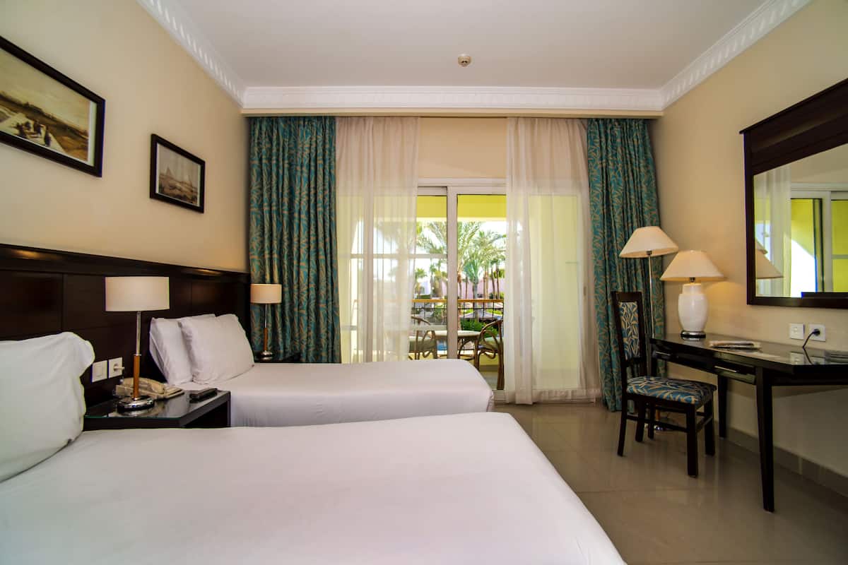 A hotel room with two beds, a desk, a chair, a lamp, a phone, and a window with curtains.