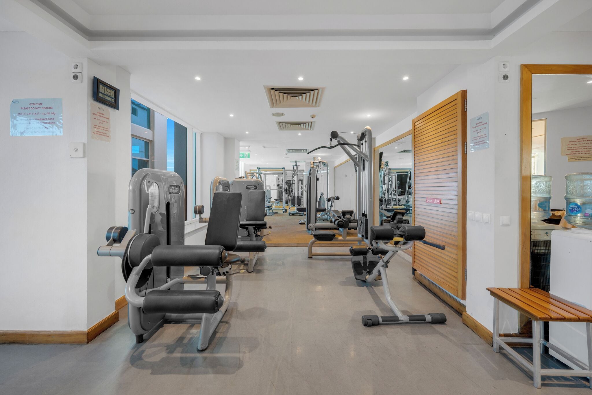 A gym with various exercise machines, a wooden bench, and a mirrored wall.