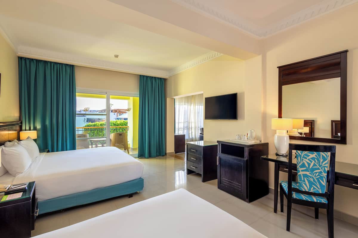 A hotel room with a bed, desk, chair, TV, and a balcony with curtains.