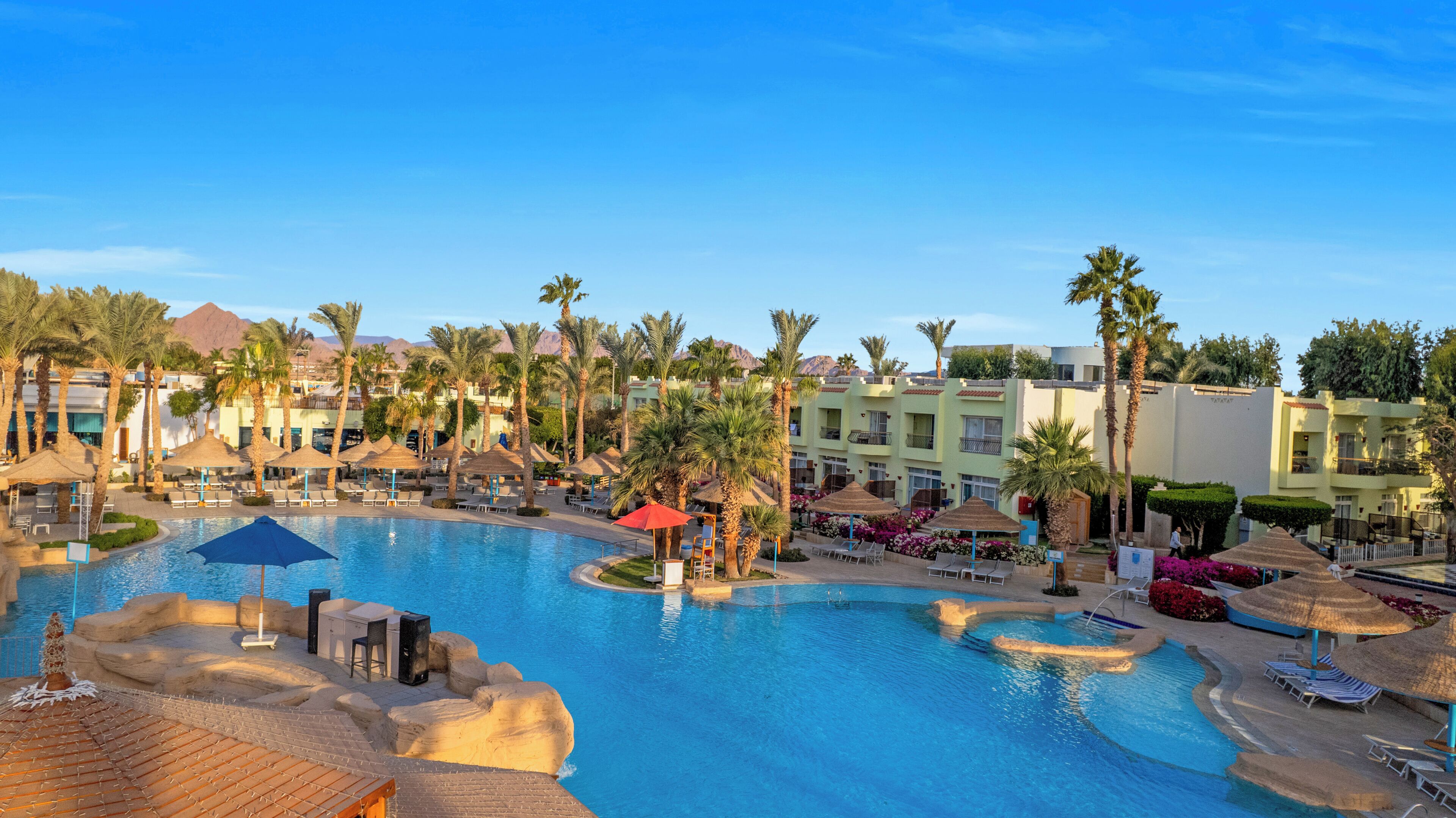 Un complexe hôtelier doté d’une grande piscine, de palmiers et de bâtiments d’hôtel.