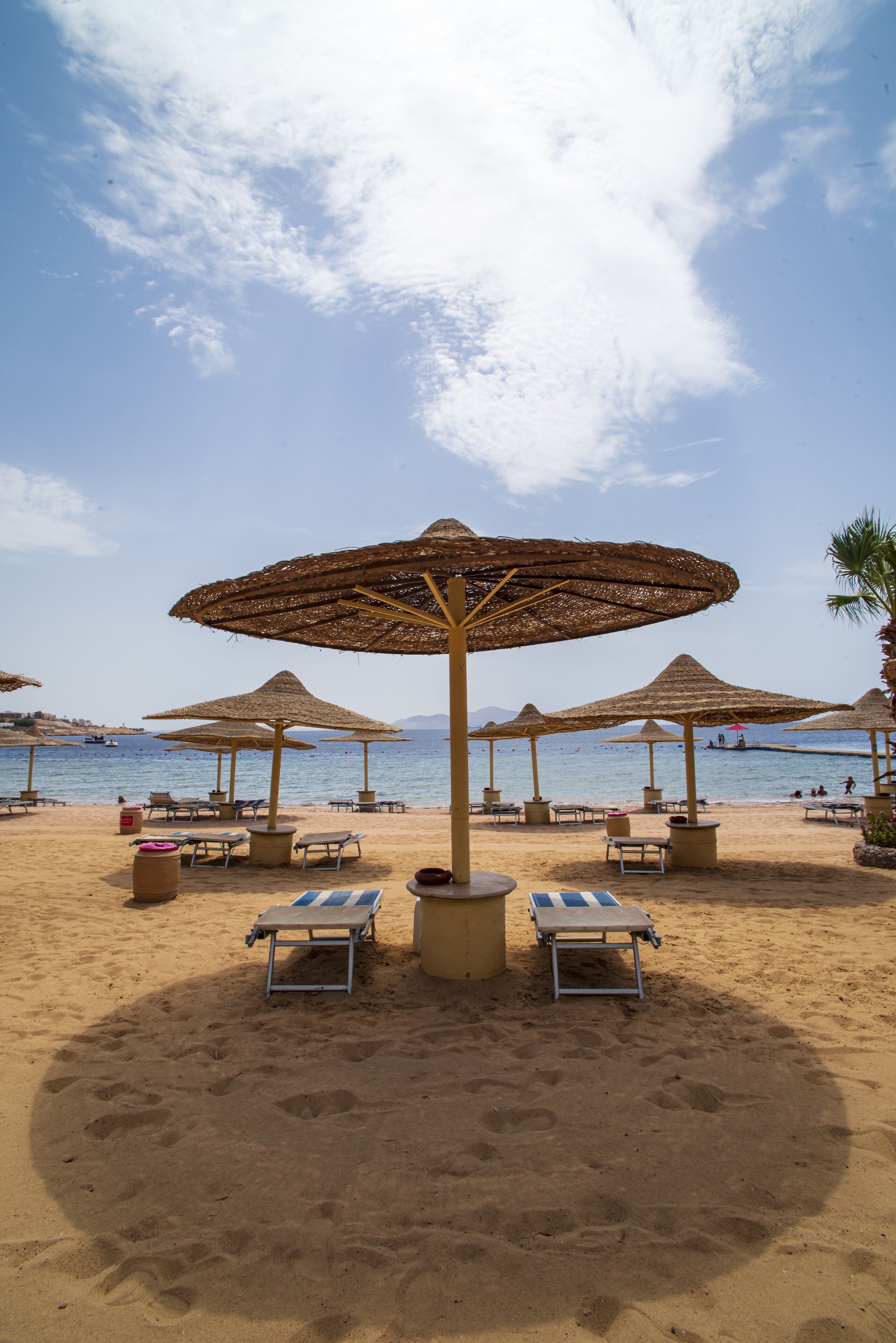 A beach with sun loungers and thatched umbrellas.