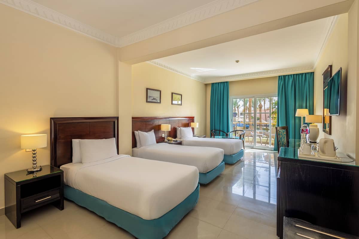 A hotel room with two beds, a nightstand with a lamp, a desk with a lamp, and a view of the outdoors.