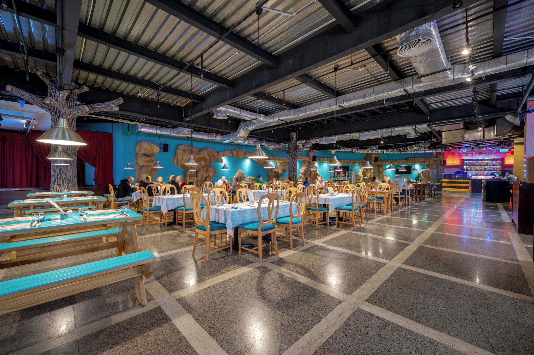 A spacious restaurant with high ceilings, exposed ductwork, and a mix of wooden and metal furniture.