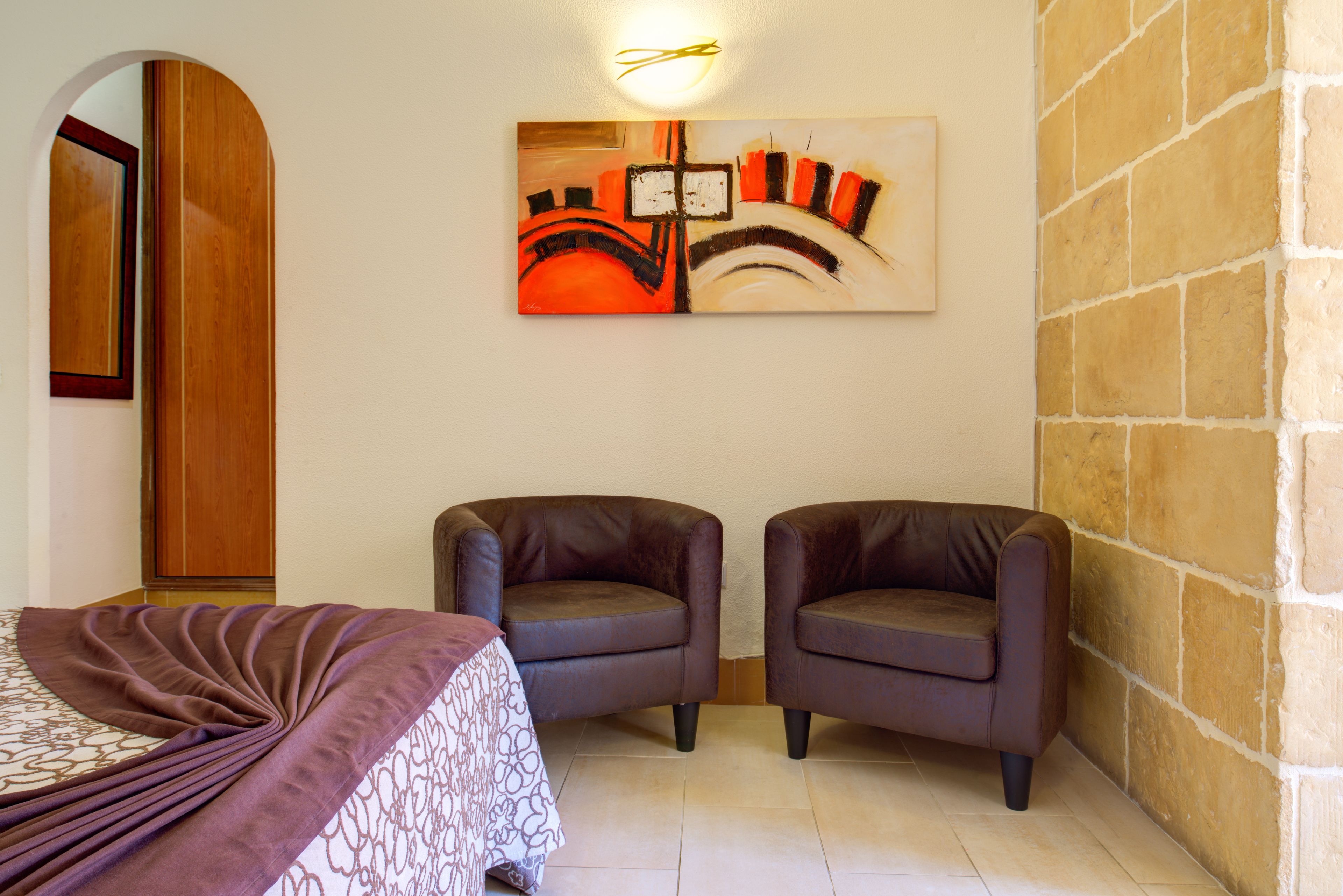A room with a bed, two armchairs, a painting on the wall, and a wooden wardrobe.