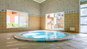 Una amplia piscina interior con paredes y suelo de baldosas, rodeada de ventanas y puertas.