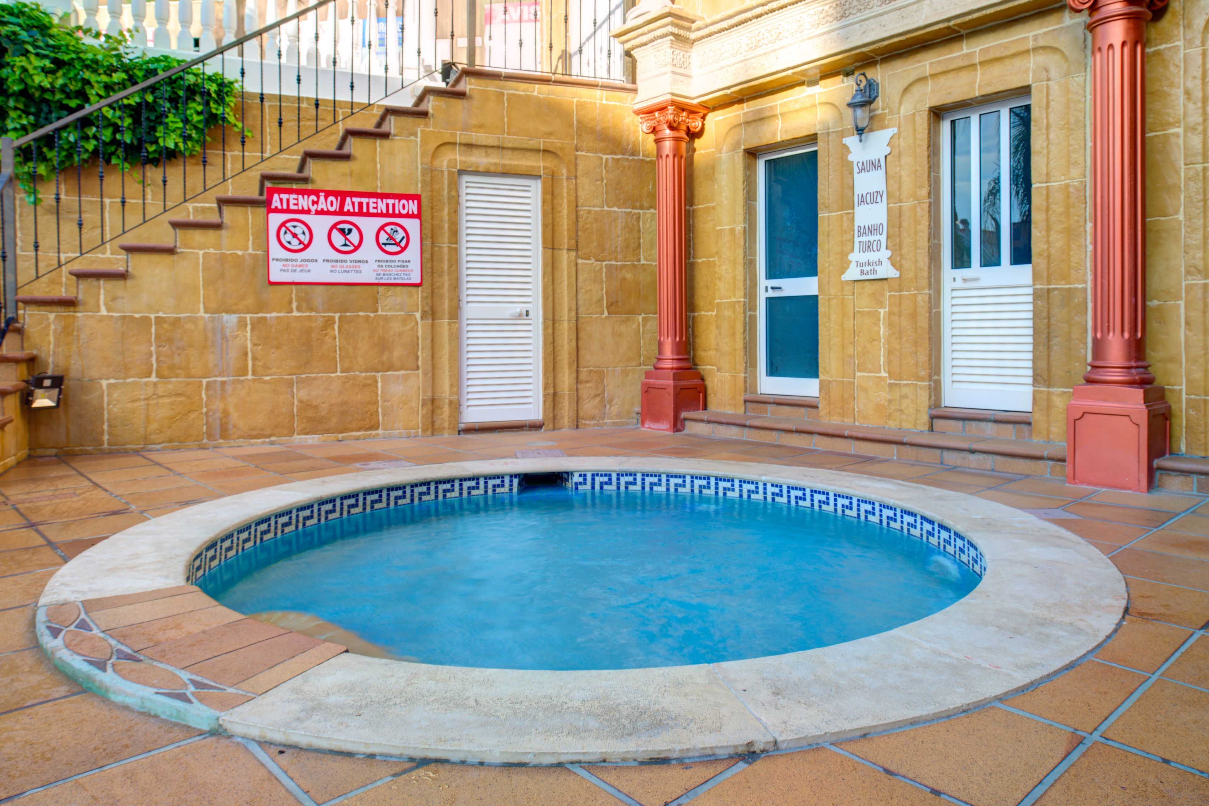 A swimming pool with a tiled edge, a sign indicating no smoking, and a building entrance with a sign for a sauna and Turkish bath.