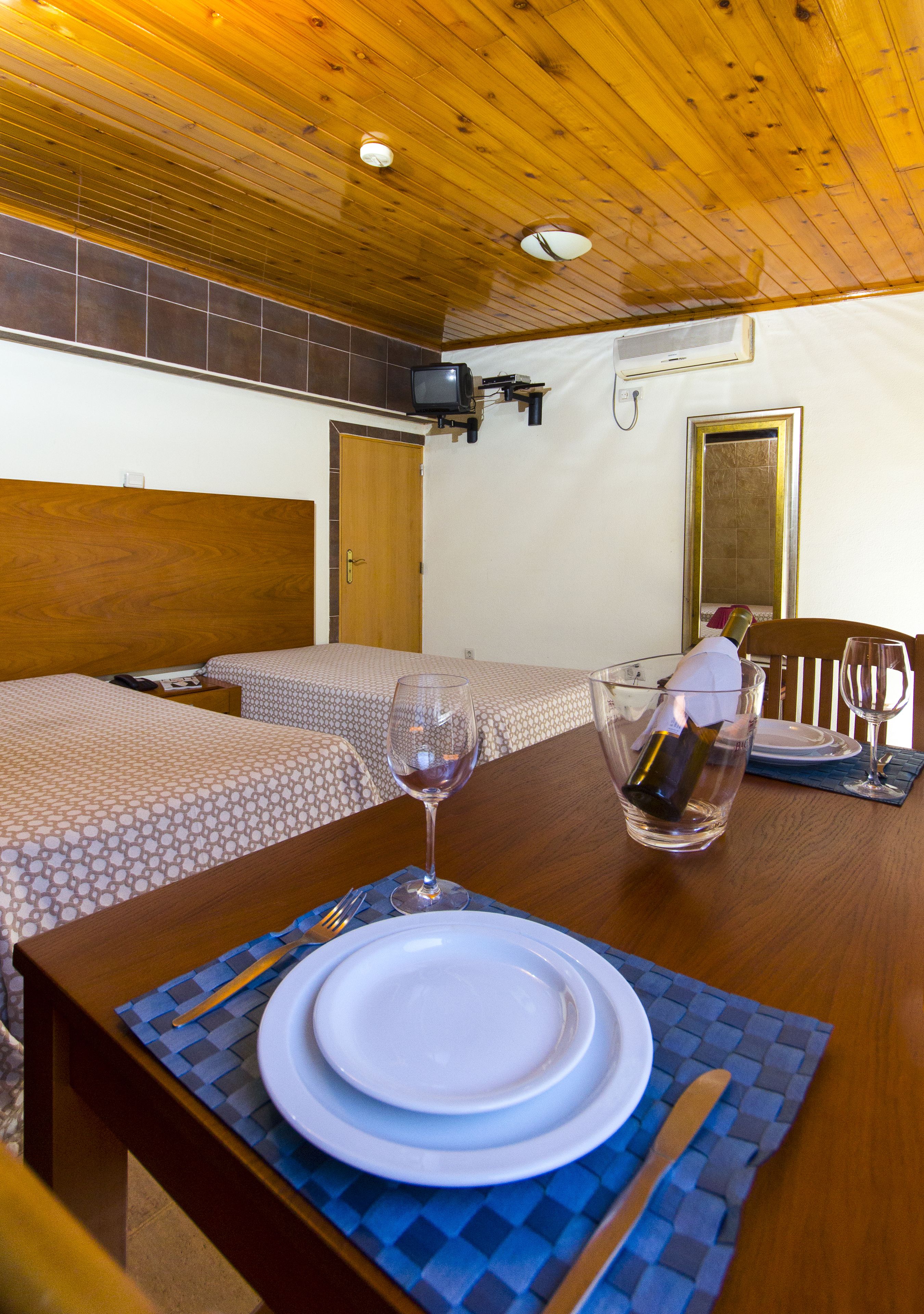A hotel room with two beds, a dining table set with plates and cutlery, a wine glass, and a bottle of wine in a glass.