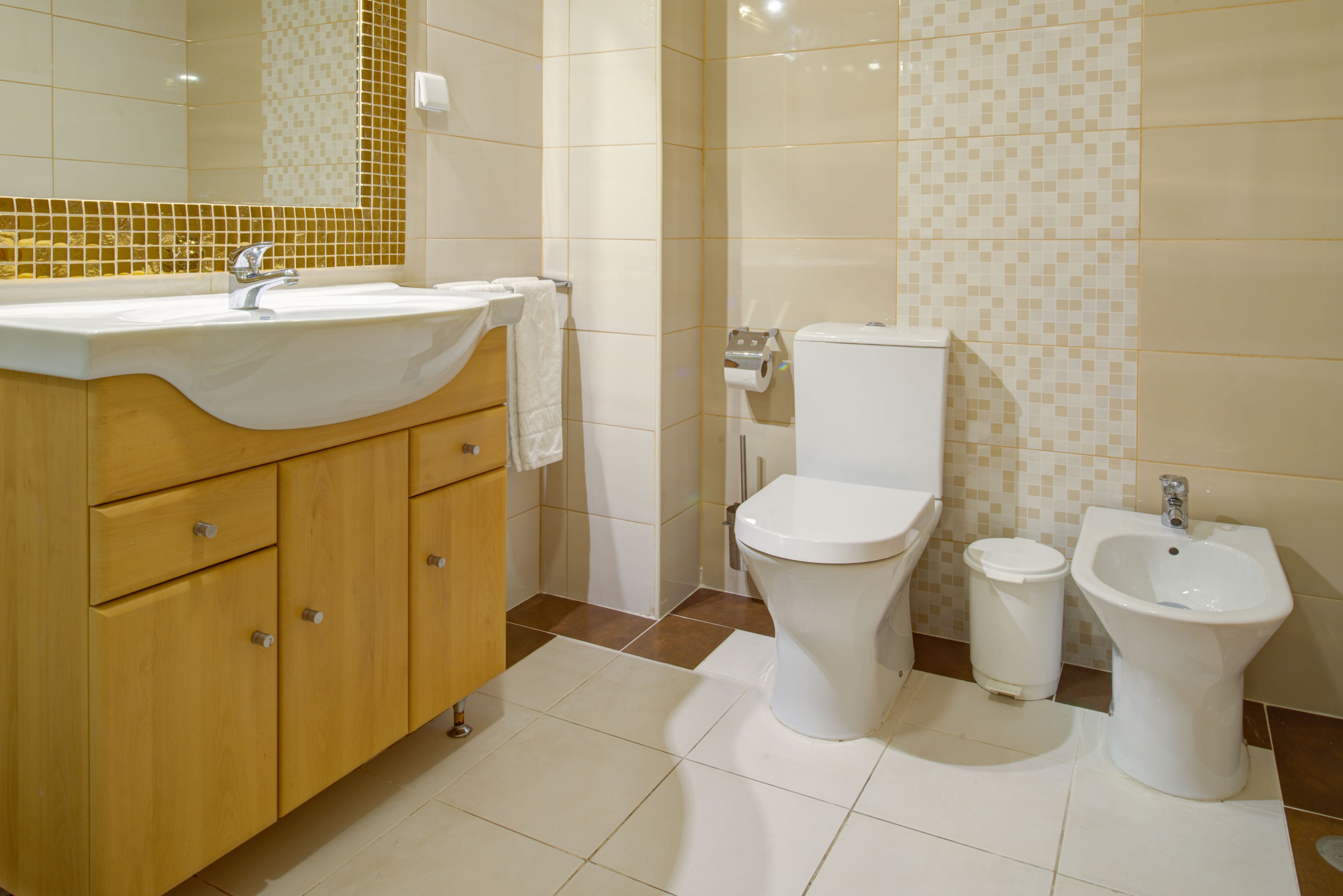 Ein Badezimmer mit Waschbecken, Toilette, Bidet und Holzschränken.