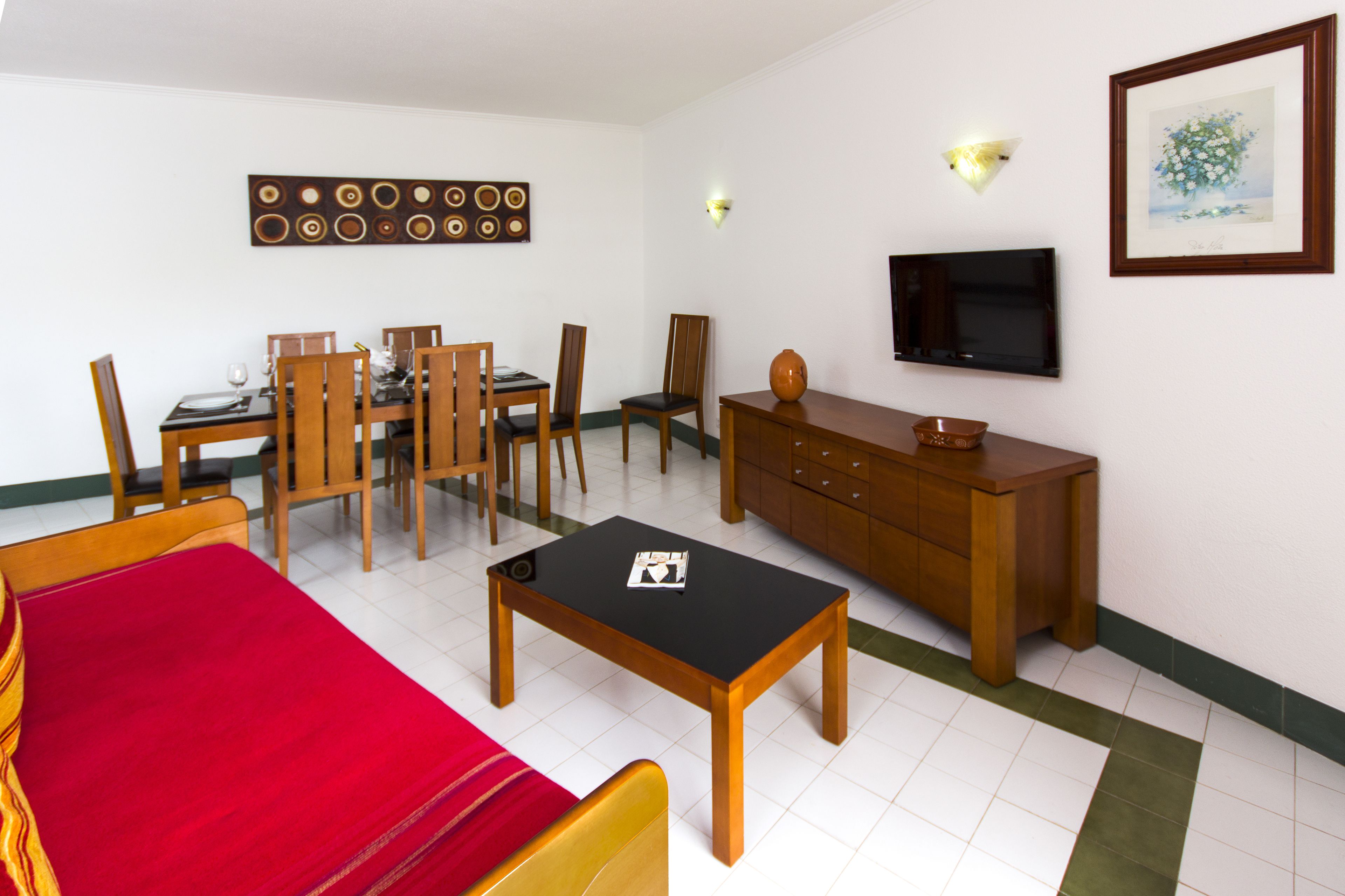 A hotel room with a dining area, a sofa, a TV, and a cabinet.
