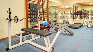 Een sportschool met trainingsapparatuur, waaronder een bank, gewichten en een loopband.
