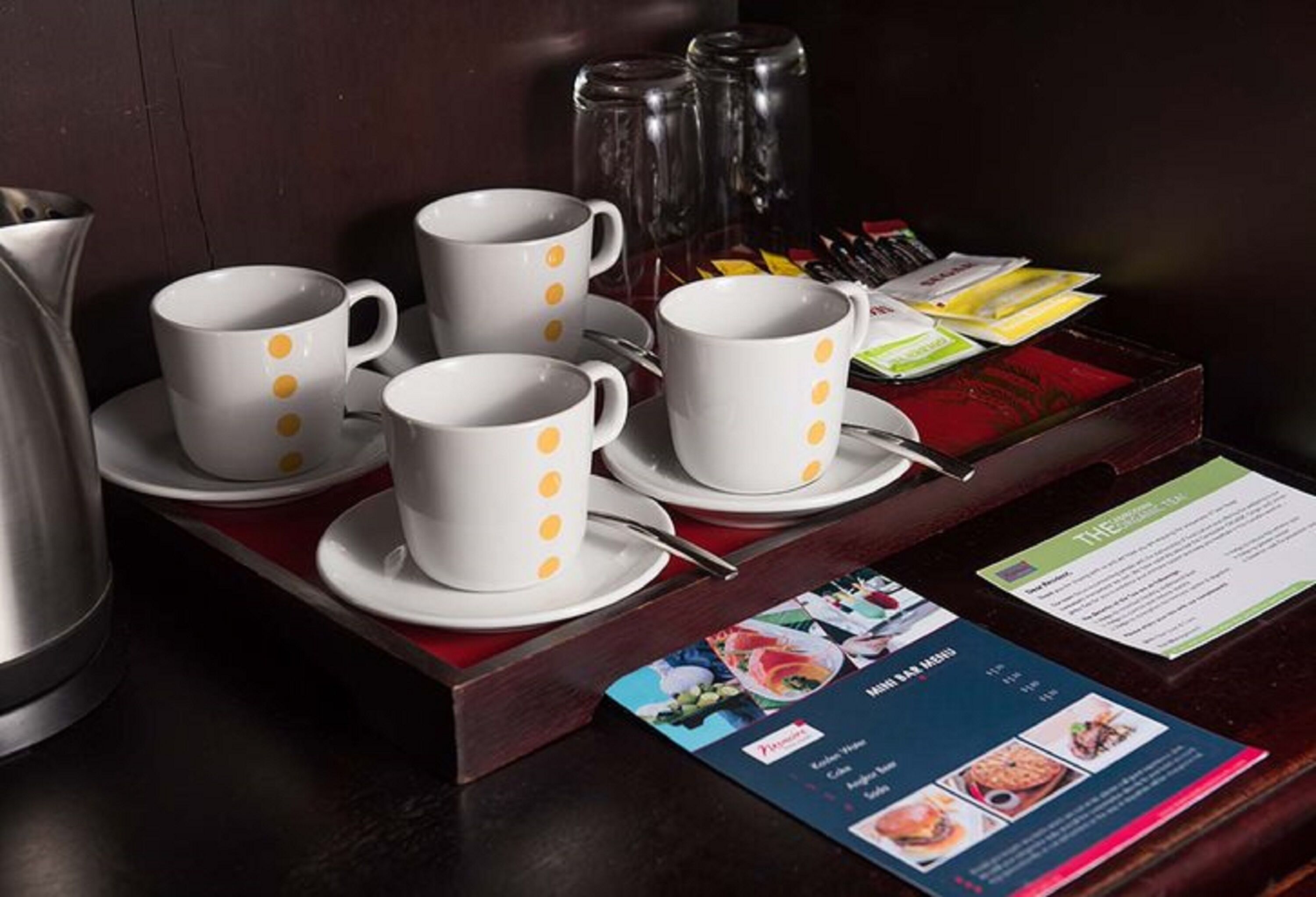 A breakfast buffet setup with white cups with yellow dots, a menu, and condiments.