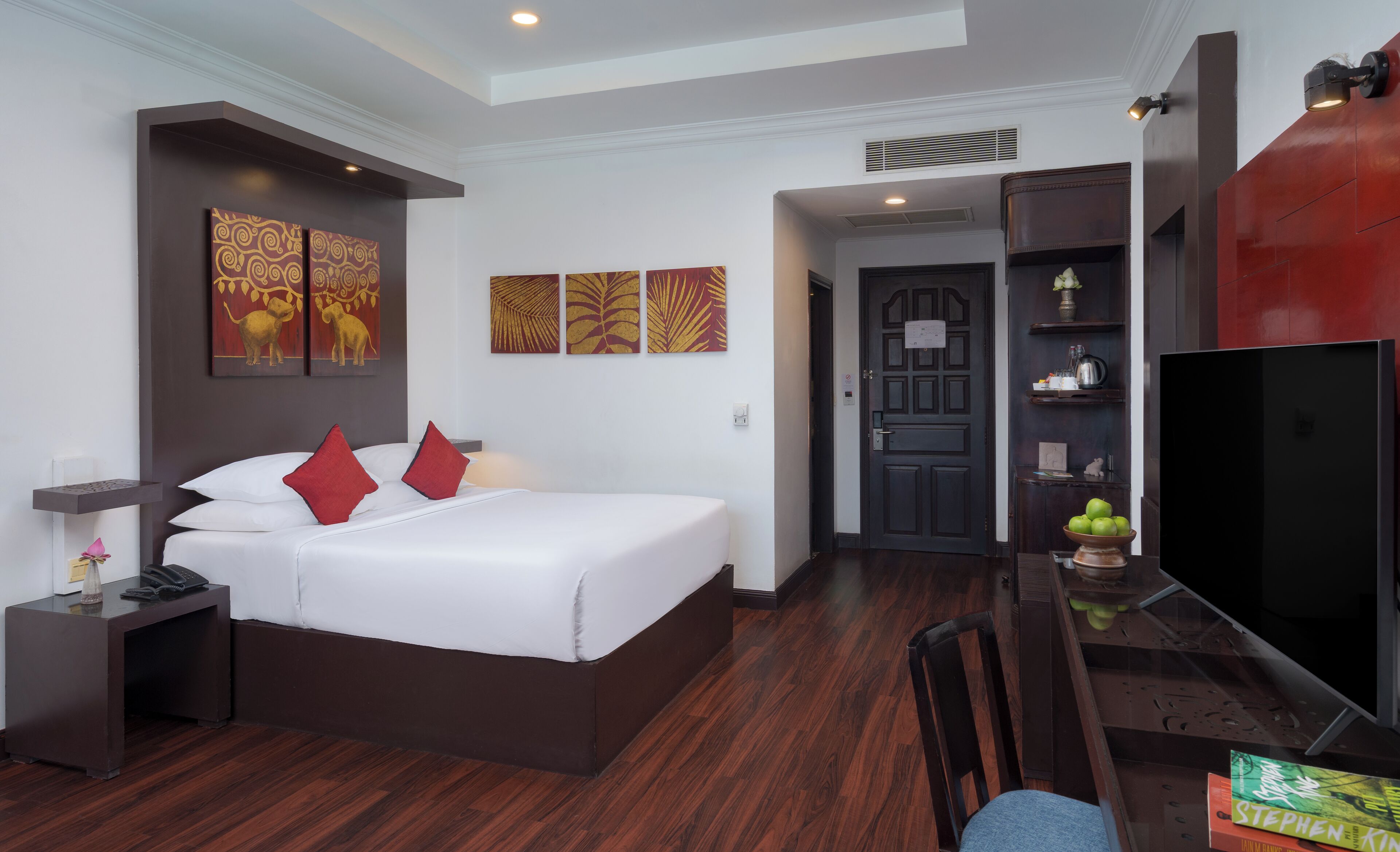 A hotel room with a large bed, a desk with a computer, a TV, and artwork on the walls.