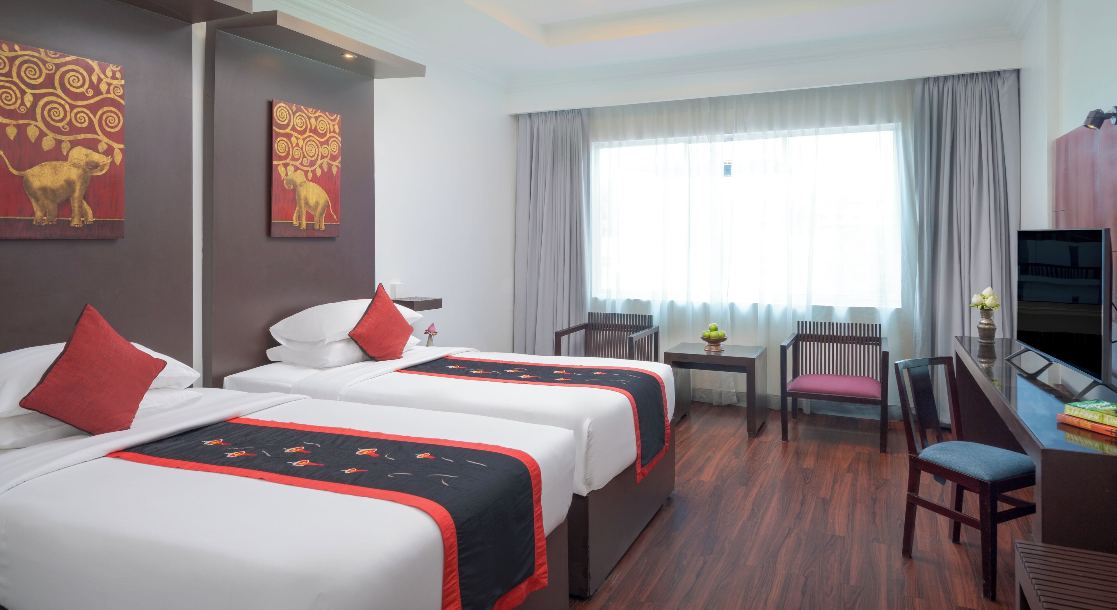 A hotel room with two beds, a desk, a chair, a TV, and a large window with curtains.