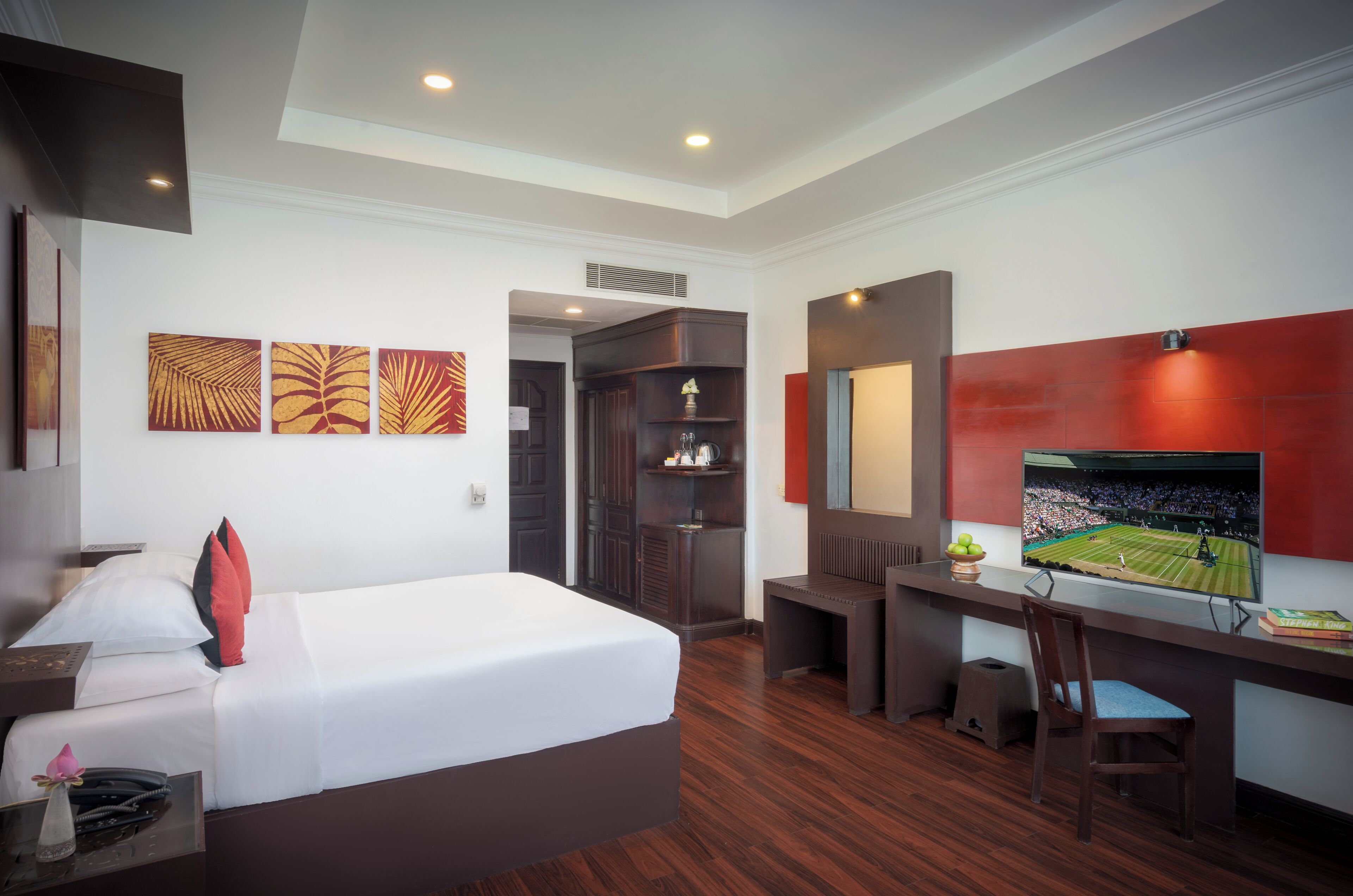 A hotel room with a bed, desk, TV, and artwork on the wall.