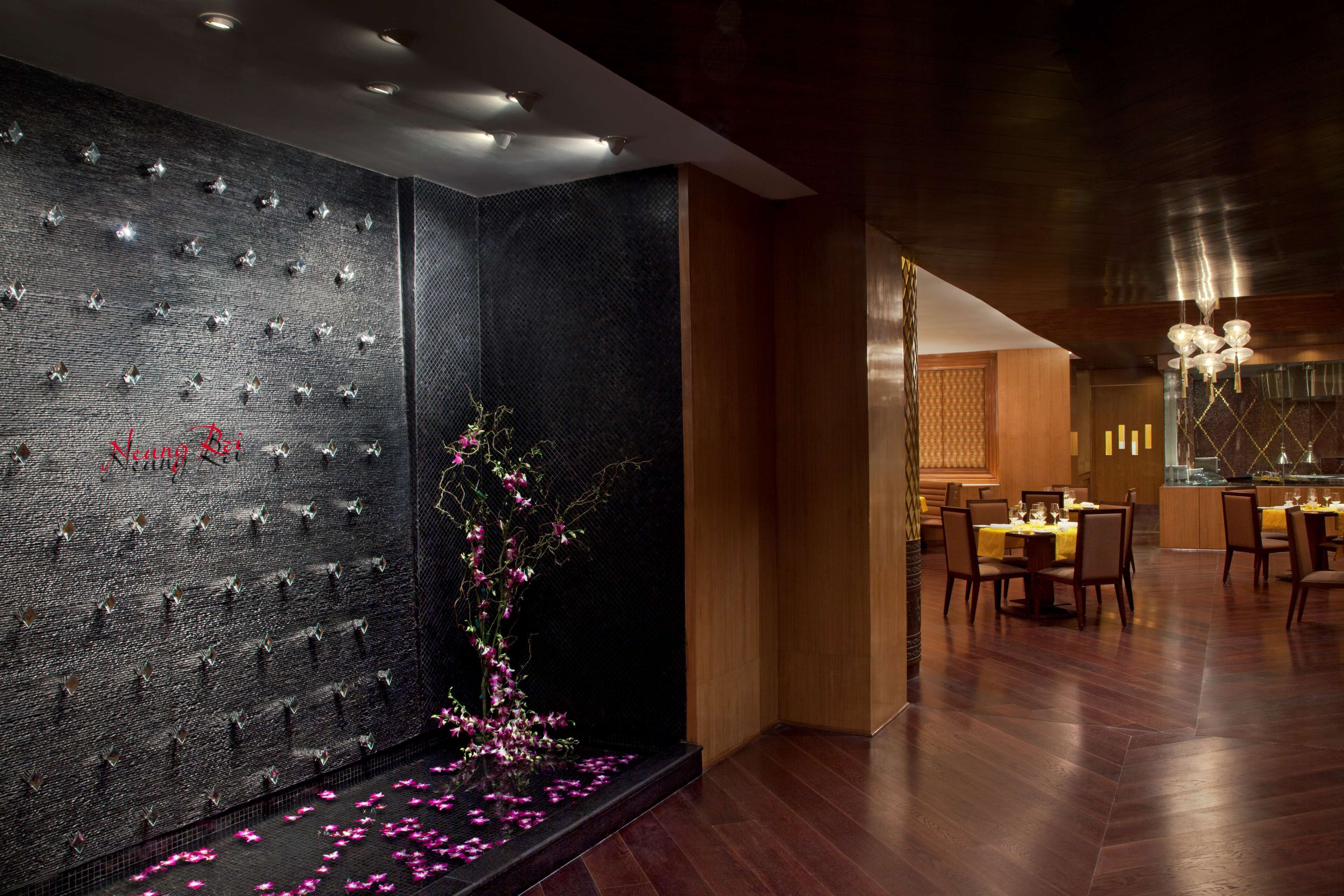 Een modern interieur met een donkere, structuurrijke muur, een bloemstuk en een eetgedeelte met houten vloeren en tafels.