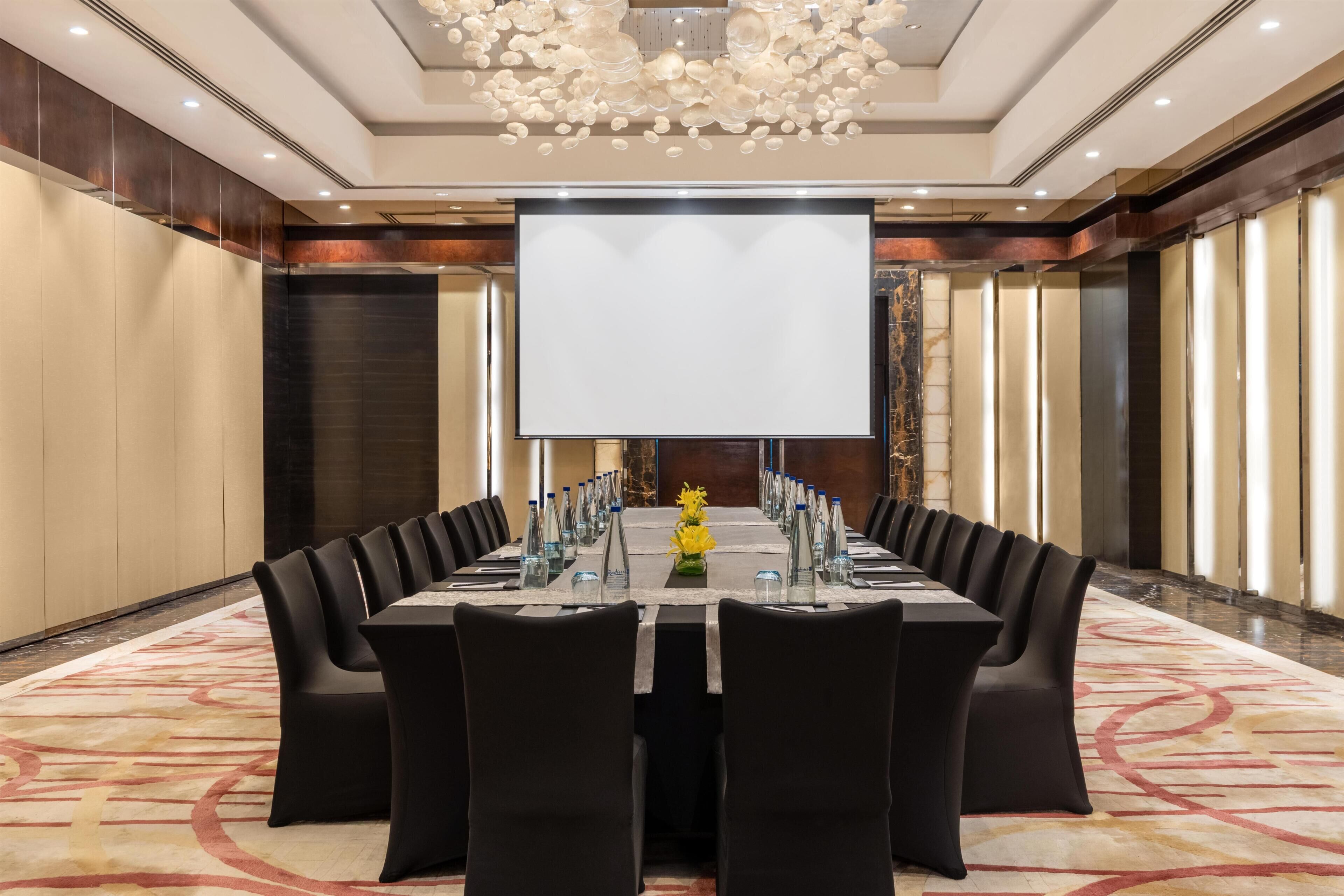A conference room with a large table, chairs, a projector screen, and a chandelier.