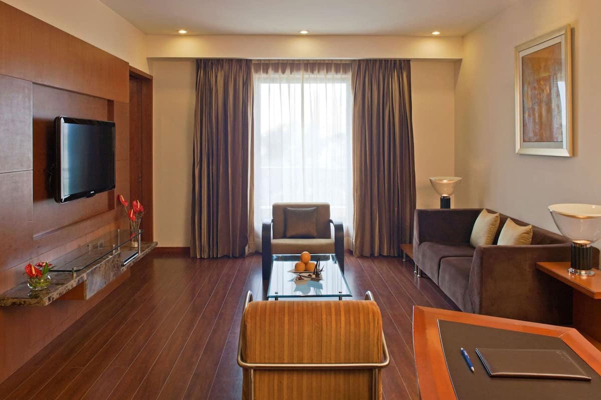 Habitación de hotel con televisor de pantalla plana, sofá, sillón, mesa de centro y escritorio con lámpara.