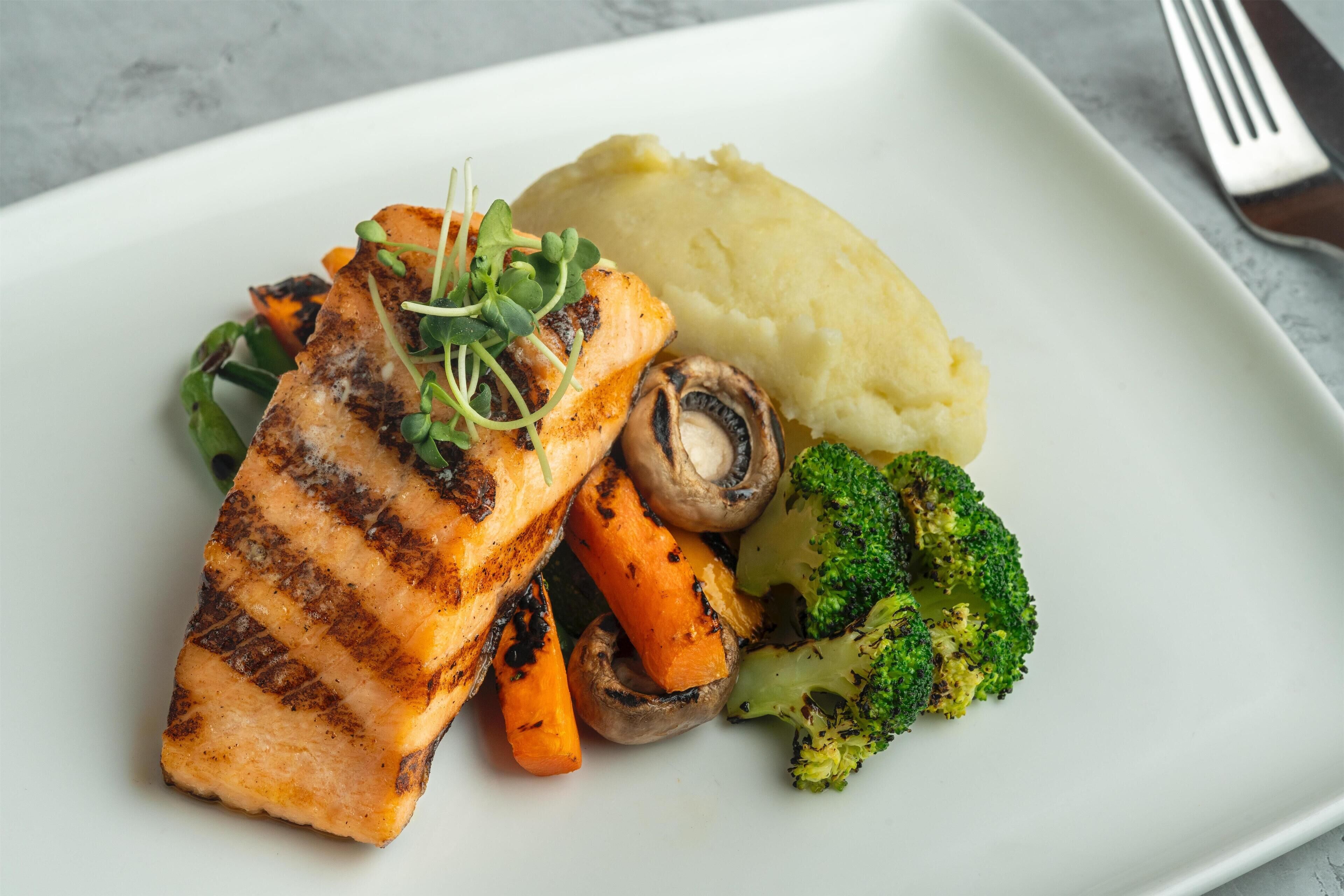 A plate with grilled salmon, mashed potatoes, carrots, and broccoli.