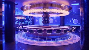 Un espace bar avec des sièges disposés en cercle, un lustre central et un mur orné de motifs lumineux circulaires.