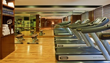 Una palestra con diverse tapis roulant, attrezzature per esercizi e un pavimento in legno.