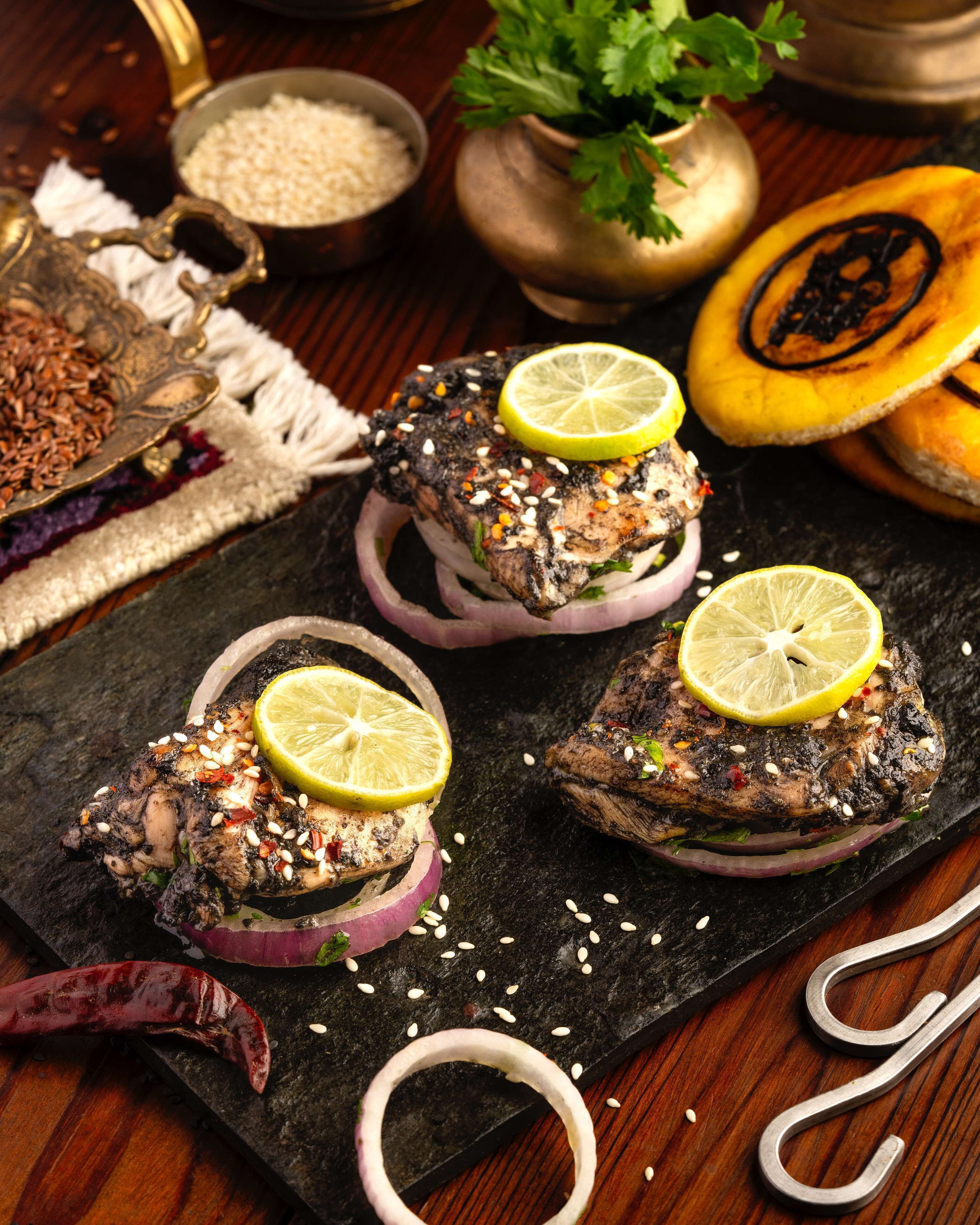 Un plat de viande grillée, garni de graines de sésame et de tranches de citron, servi sur une assiette en ardoise foncée.