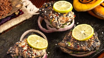 A dish of grilled meat topped with sesame seeds and lemon slices, served on a dark slate plate.