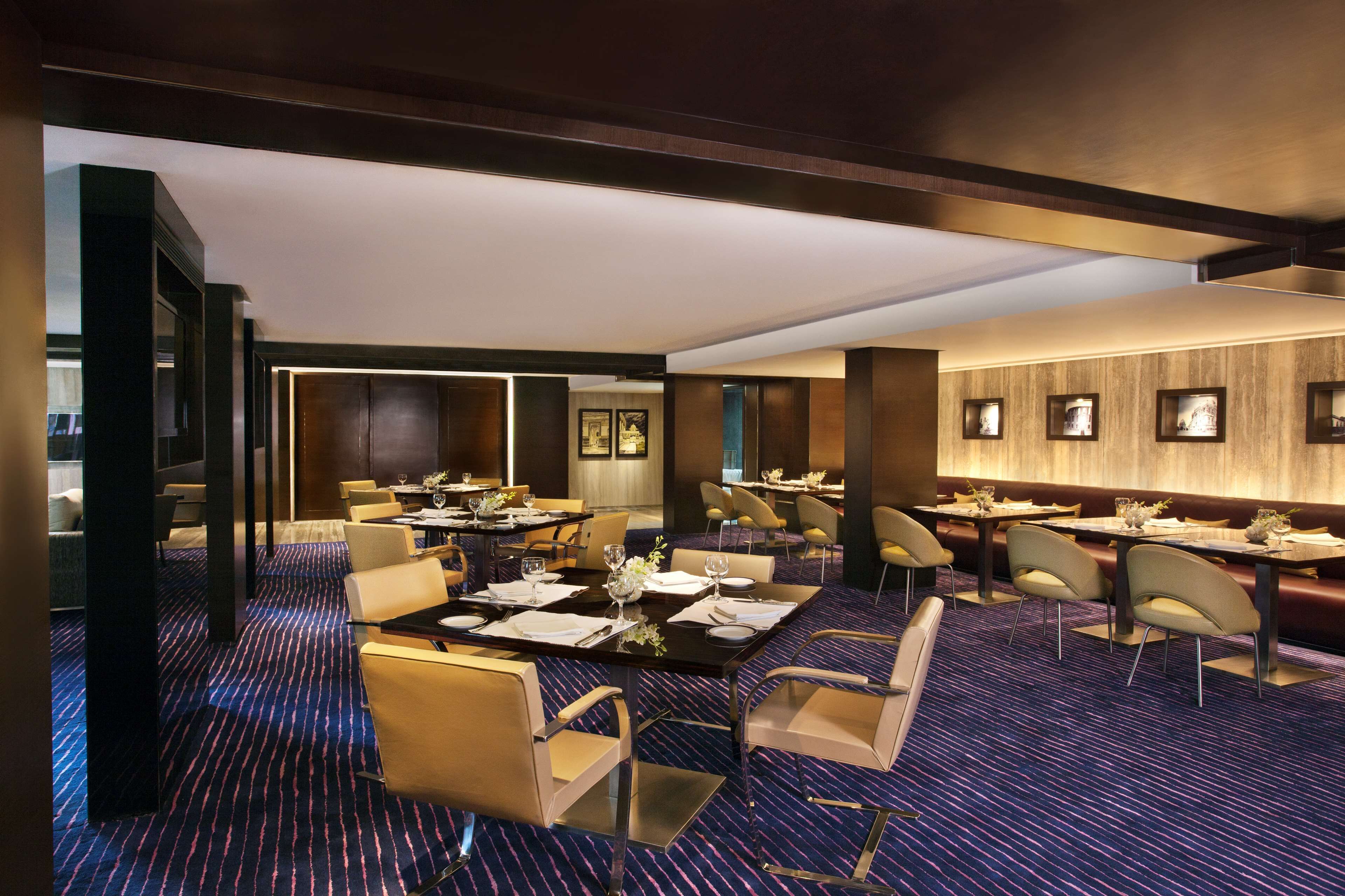 A hotel dining area with multiple tables and chairs, a patterned carpet, and framed artwork on the walls.