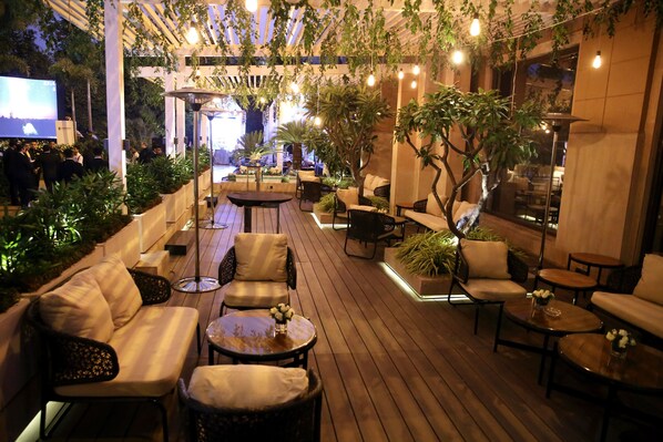 Un espacio exterior con piso de madera, asientos acolchados y plantas en macetas.
