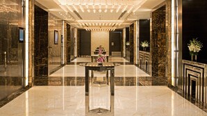 Un hall d’entrée luxueux avec un sol en marbre, une table centrale ornée d’un vase de fleurs et un lustre moderne.
