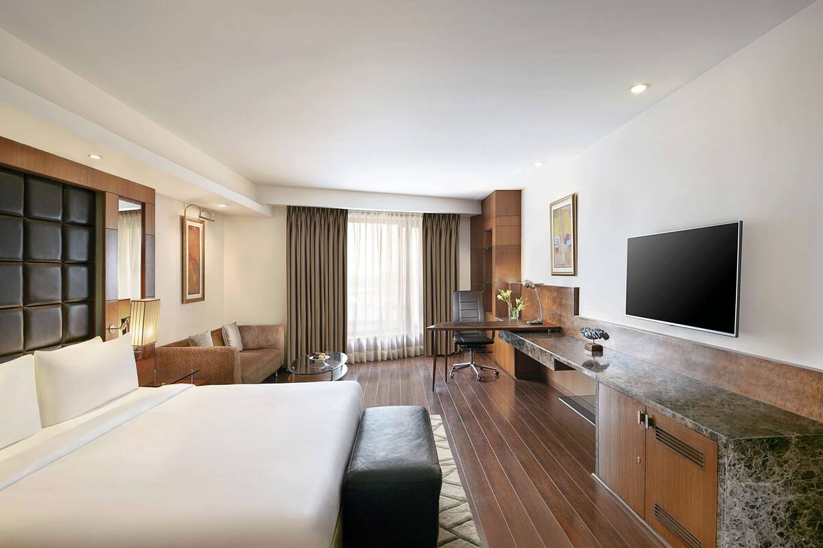 Habitación de hotel con una cama grande, un escritorio, una silla, un televisor y una ventana con cortinas.