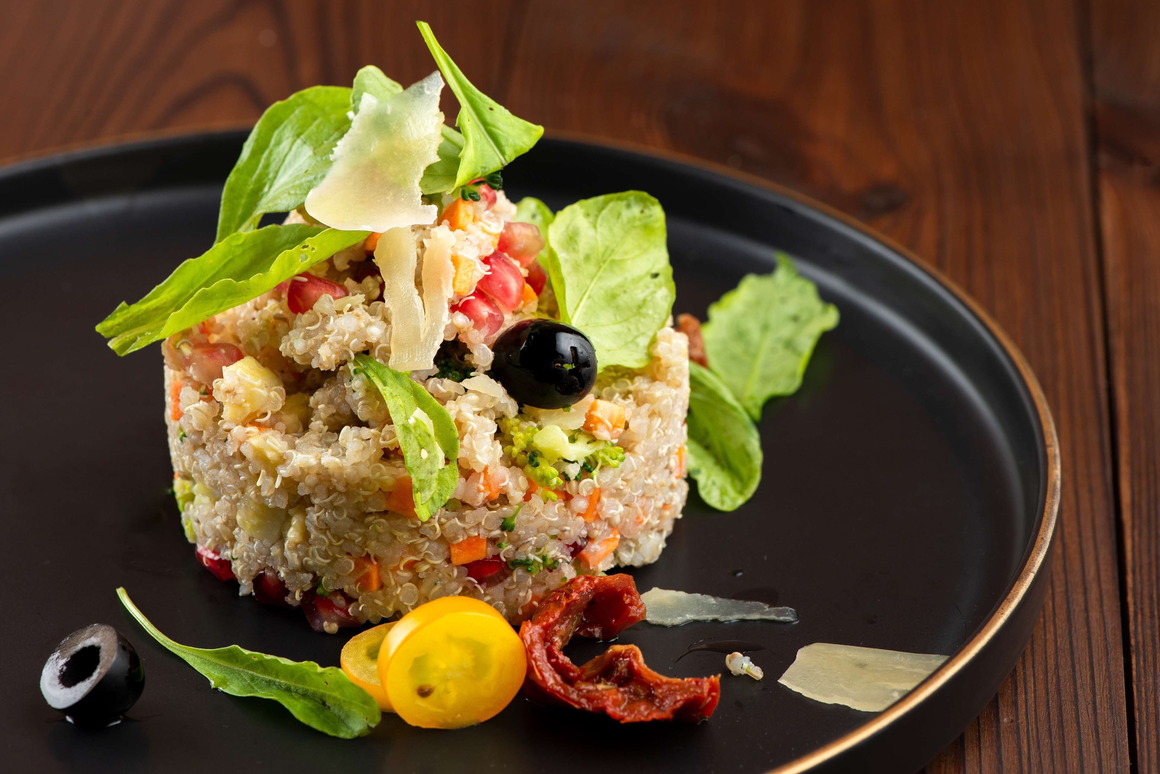 A dish with quinoa, vegetables, and garnishes on a black plate.